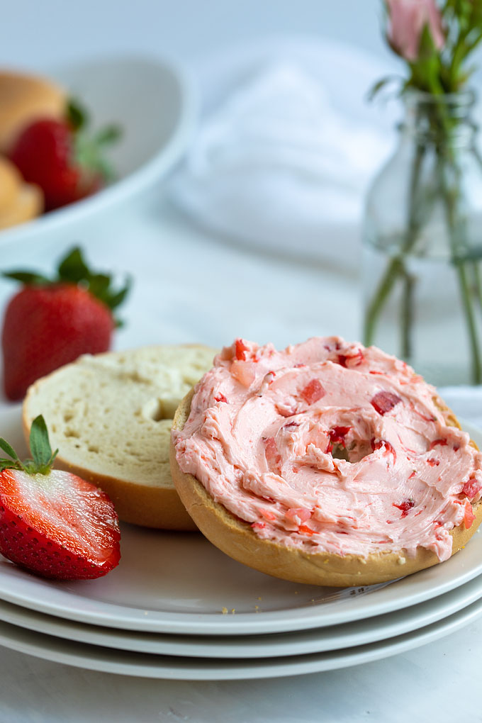 An open-faced bagel spread with strawberry butter on a round white plate.