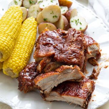 Overhead view of a rack of ribs, 3 ears of corn on the cob and baby red potatoes on a white oval serving platter