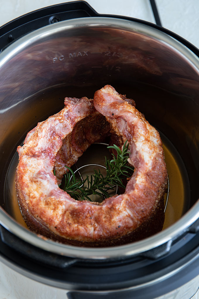 Overhead view of a rack of pork ribs on their side formed into a circle shape in the insert of a pressure cooker