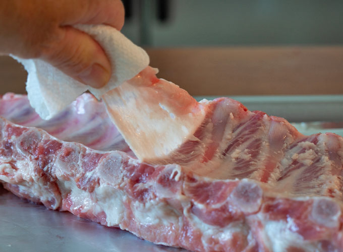 The back side of a rack of pork ribs with the membrane being pulled away by hand