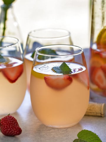 White wine sangria with strawberries and lemonade in 3 wine glasses beside a glass pitcher