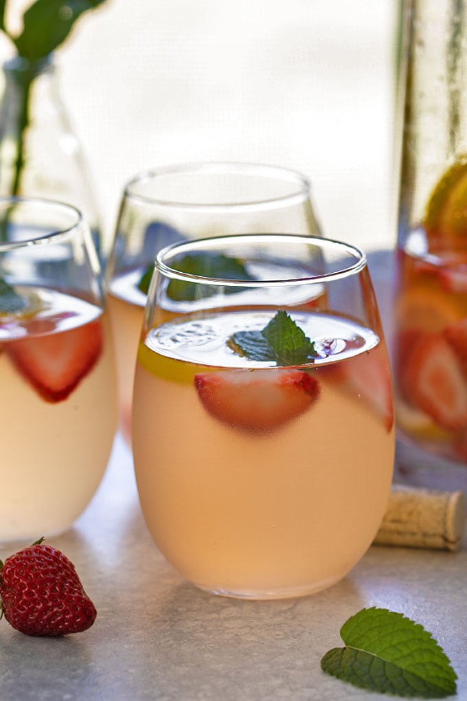 White wine sangria with strawberries and lemonade in 3 wine glasses beside a glass pitcher