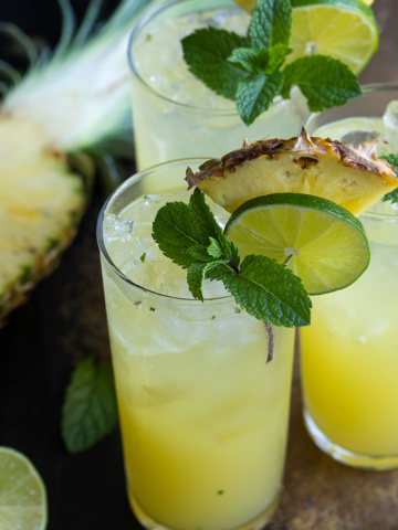 3 Pineapple Mojitos garnished with fresh pineapple, lime and mint