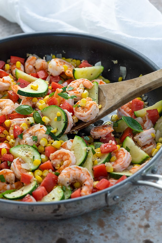 Shrimp Stir-Fry with corn and zucchini in a large skillet with a wooden serving spoon