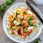 Overhead view of shrimp, corn and zucchini stir-fry over rice in a bowl with chopsticks
