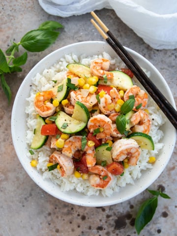Overhead view of shrimp, corn and zucchini stir-fry over rice in a bowl with chopsticks