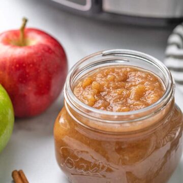 Applesauce in a mason jar beside fresh apples with a slow cooker in the background