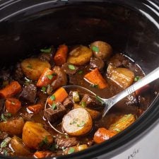 Balsamic beef stew in an oval slow cooker with a ladle