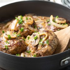 Hamburger steak patties with gravy, mushrooms and onions in a skillet