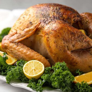 A roasted turkey on a white platter garnished with kale and fruit