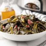 Collard greens in a white bowl with a slow cooker in the background