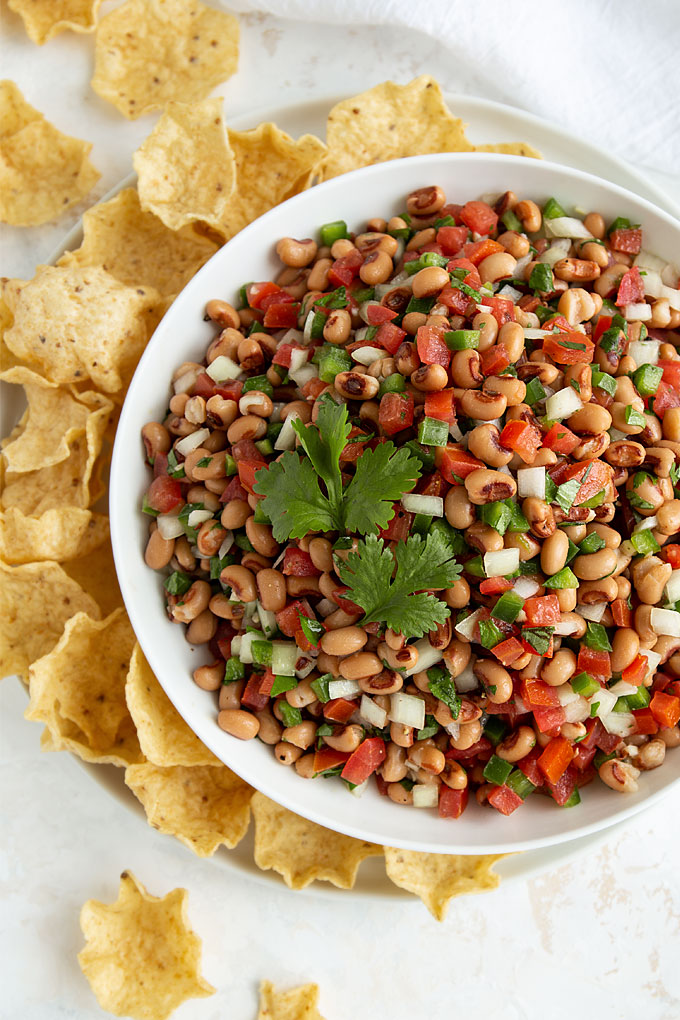Overhead view of black-eyed pea salsa in a round white bowl beside tortilla chips