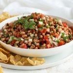 Black-eyed pea salsa in a white bowl on a white plate with tortilla chips