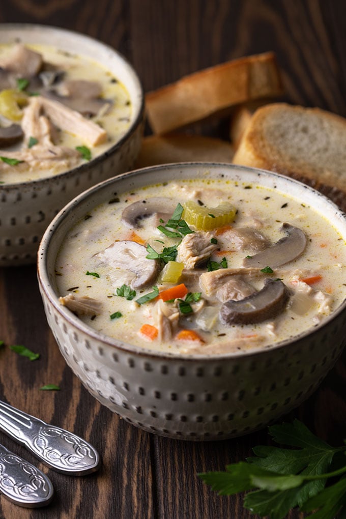 Two bowls of creamy leftover turkey soup with mushrooms beside spoons and sliced bread