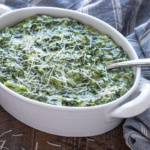 Creamed spinach in a white oval baking dish with a serving spoon.