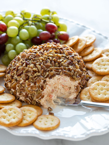 A shrimp cheese ball on a platter with a cheese spreader, crackers and grapes