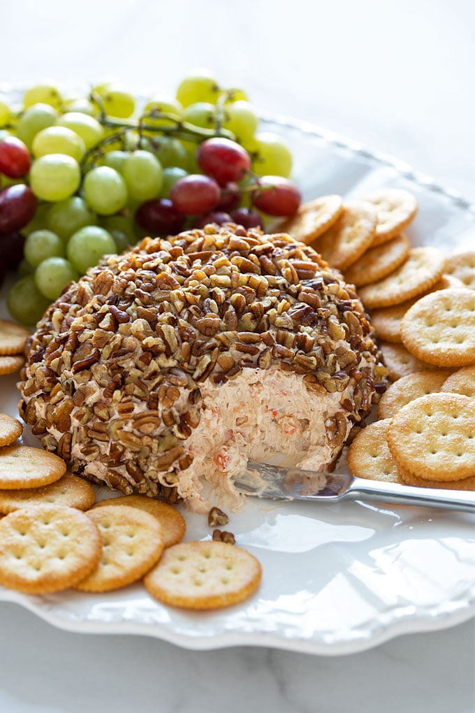 A shrimp cheese ball on a platter with a cheese spreader, crackers and grapes