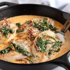 Chicken in a sun-dried tomato and spinach cream sauce in a cast iron skillet with a spatula under a piece of chicken