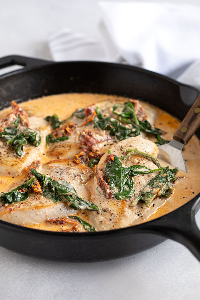 Front closeup view of creamy Tuscan chicken in a skillet with a spatula.