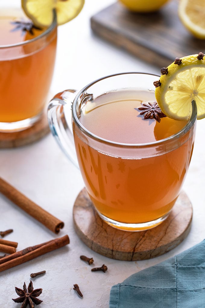 Hot toddy in a glass mug garnished with star anise and a lemon slice.