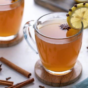 Hot toddy in a glass mug garnished with star anise and a clove-studded lemon wheel.
