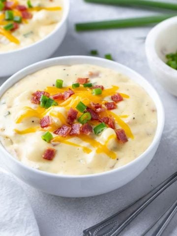 Loaded baked potato soup in a round white bowl beside 2 spoons