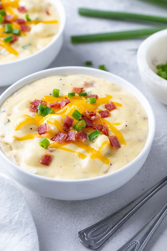 Loaded baked potato soup in a white bowl beside two spoons.