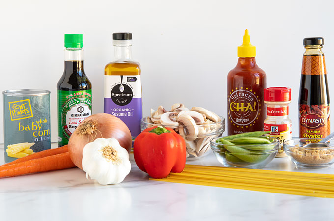Bottles of sauces, sesame oil, fresh vegetables, mushrooms, spaghetti noodles, and a bottle of ground ginger.