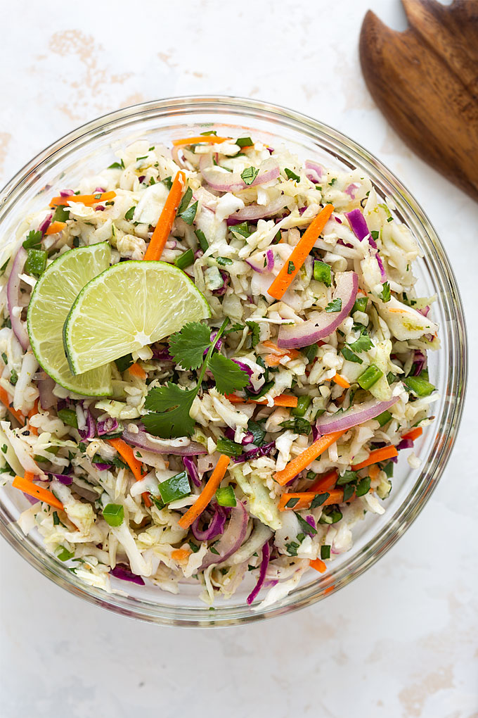 Overhead view of Mexican Coleslaw in a clear glass bowl beside a wooden server