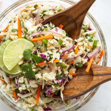 Overhead shot of Mexican coleslaw in a clear glass bowl with wooden servers