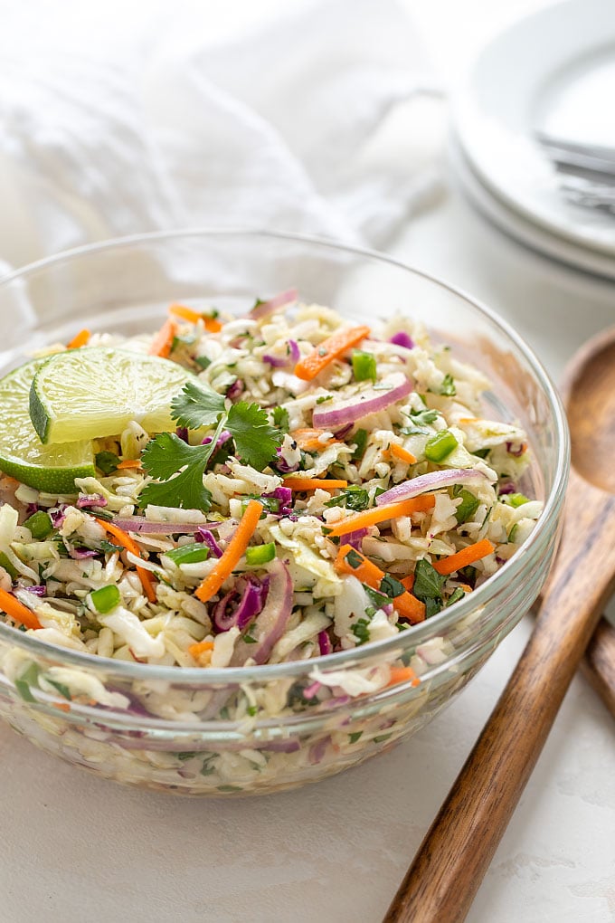 A glass bowl of Mexican coleslaw beside wooden servers.