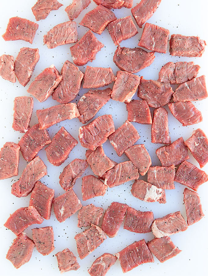 Overhead view of raw sirloin beef strips seasoned with salt and pepper on a white cutting board