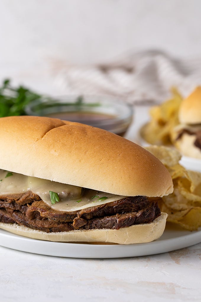 A crock pot French dip sandwich topped with melted provolone on a white plate. 