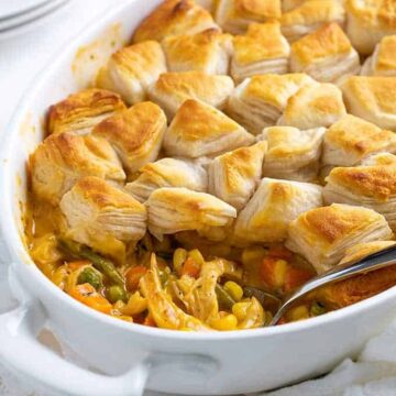 Chicken pot pie topped with canned biscuits in an oval white dish with a serving spoon.