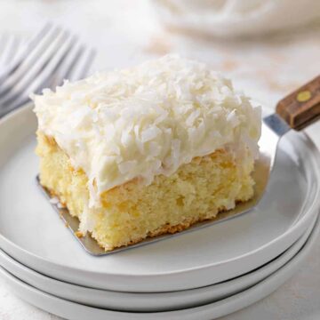A slice of coconut cake being placed on a white plate with a server.