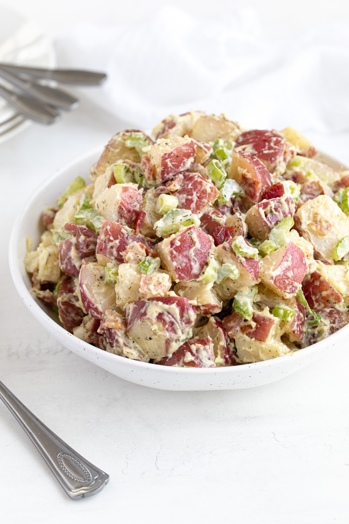A bowl of red skin potato salad by a serving spoon and a white napkin.