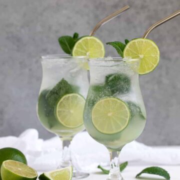 Front view of two mojitos on a white surface and a gray background.