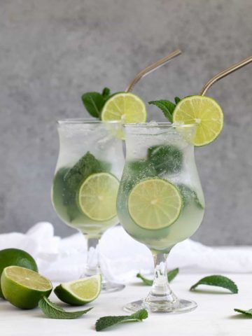 Front view of two mojitos on a white surface and a gray background.