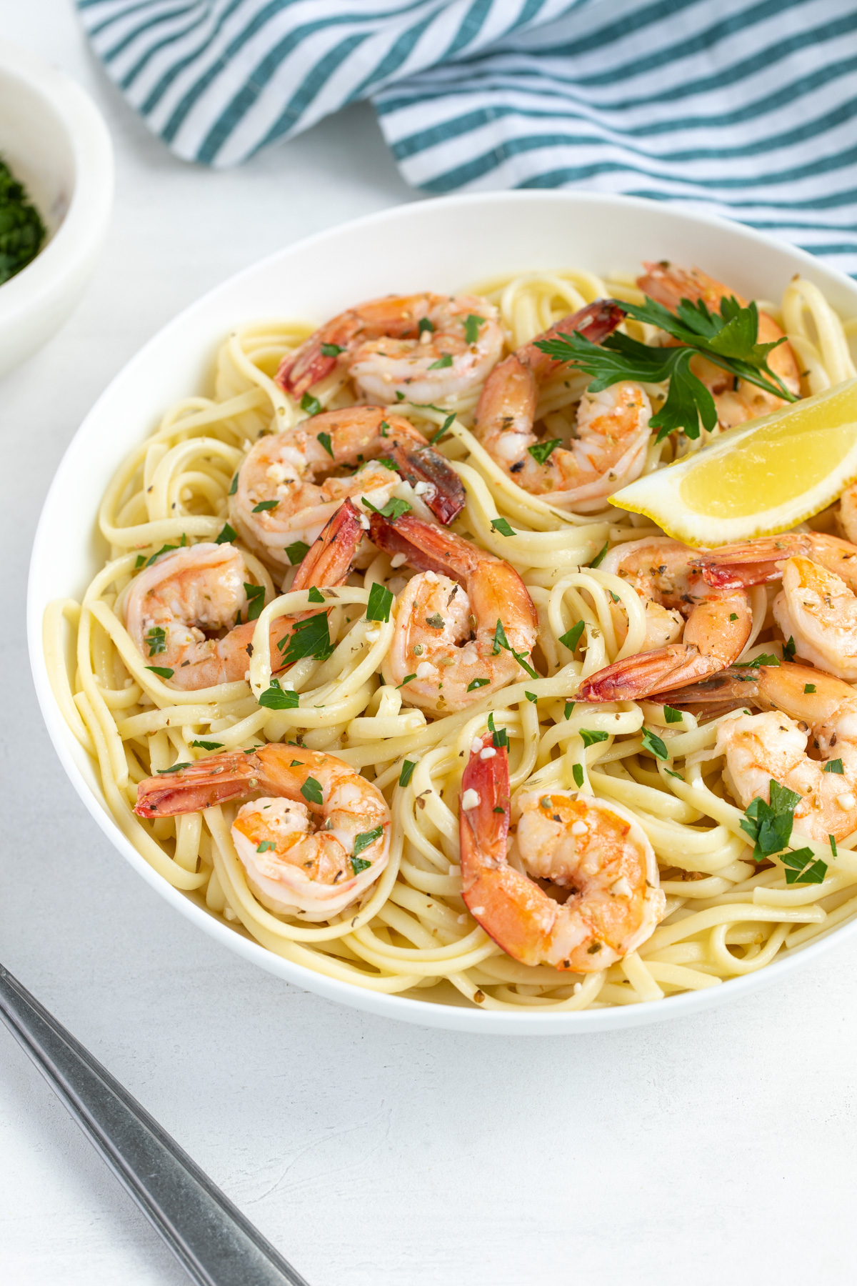 Easy shrimp scampi with pasta in a white bowl garnished with parsley and lemon.
