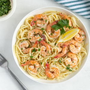 Overhead view of shrimp and pasta in a white bowl on a white surface.