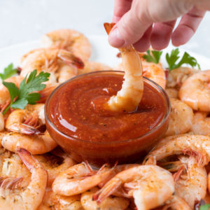 A steamed shrimp being dipped into a bowl of homemade cocktail sauce.