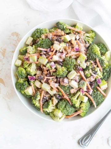 Overhead view of broccoli salad in a white bowl beside a spoon.