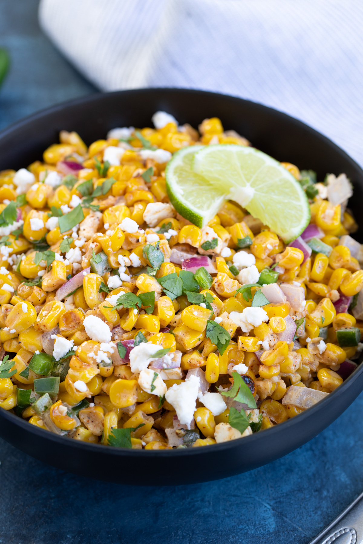 Closeup of a black bowl of corn salad topped with chopped fresh cilantro.