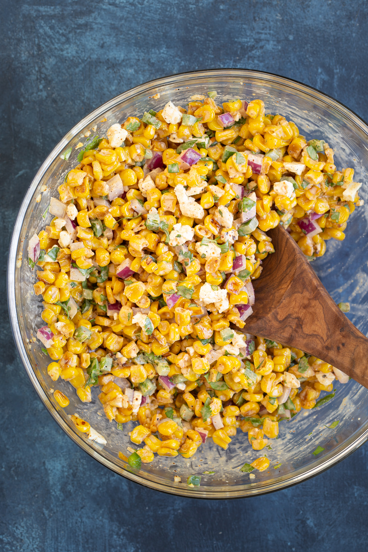 Overhead view of Mexican corn salad in a glass bowl with a wooden spoon.