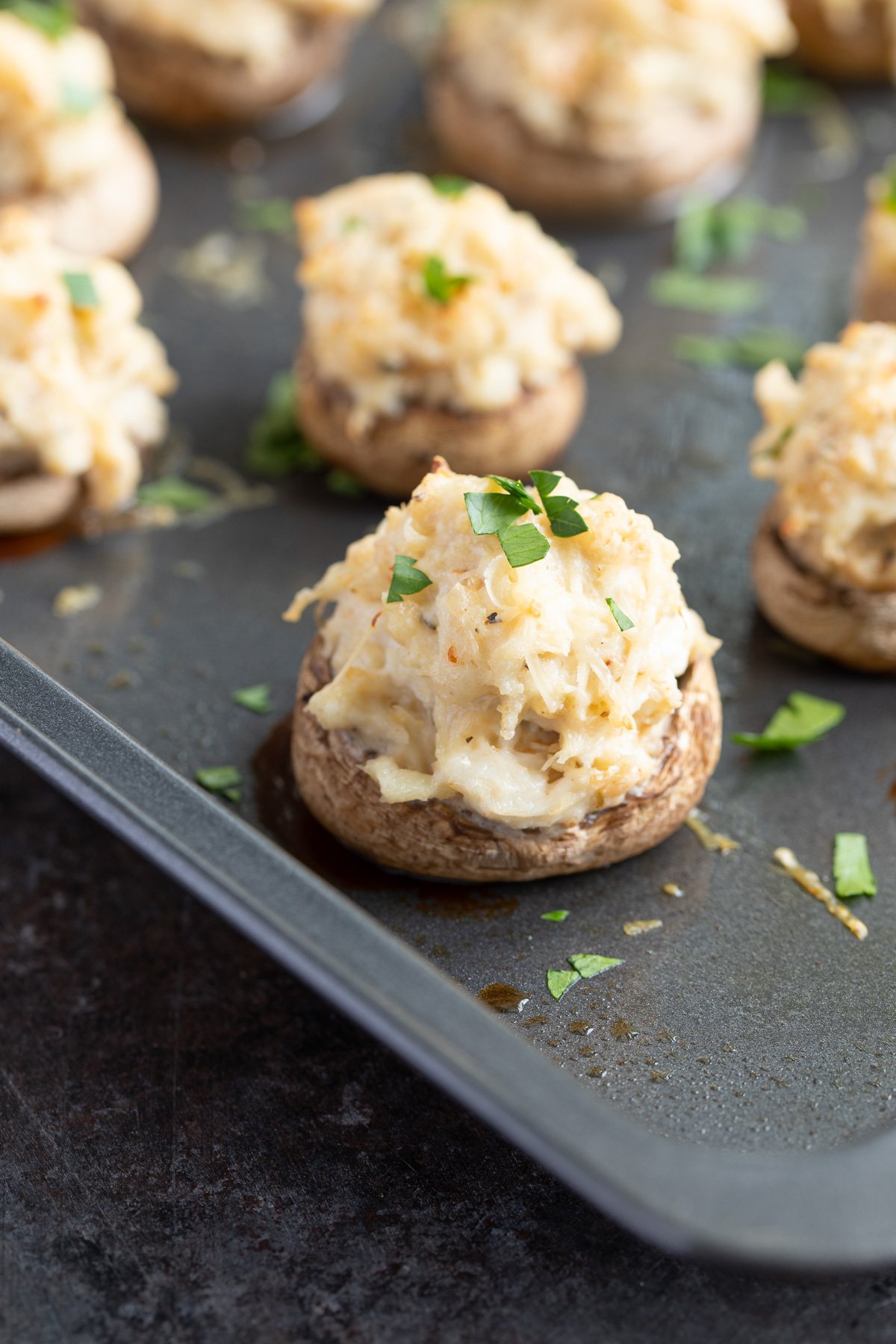 Closeup view of a stuffed mushroom sprinkled with chopped parsley on a baking sheet.