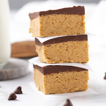 Closeup view of three stacked peanut butter bars. A glass of milk is in the background.