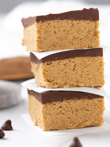 Closeup view of three stacked peanut butter bars. A glass of milk is in the background.