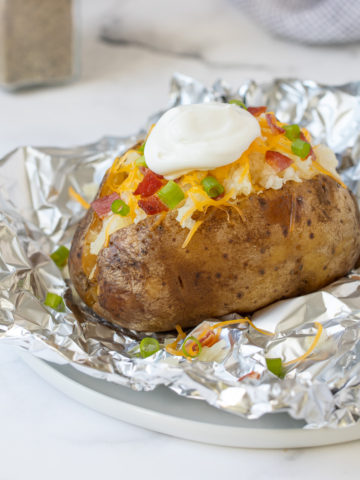 A slow cooked russet potato with toppings on top of a piece of aluminum foil.