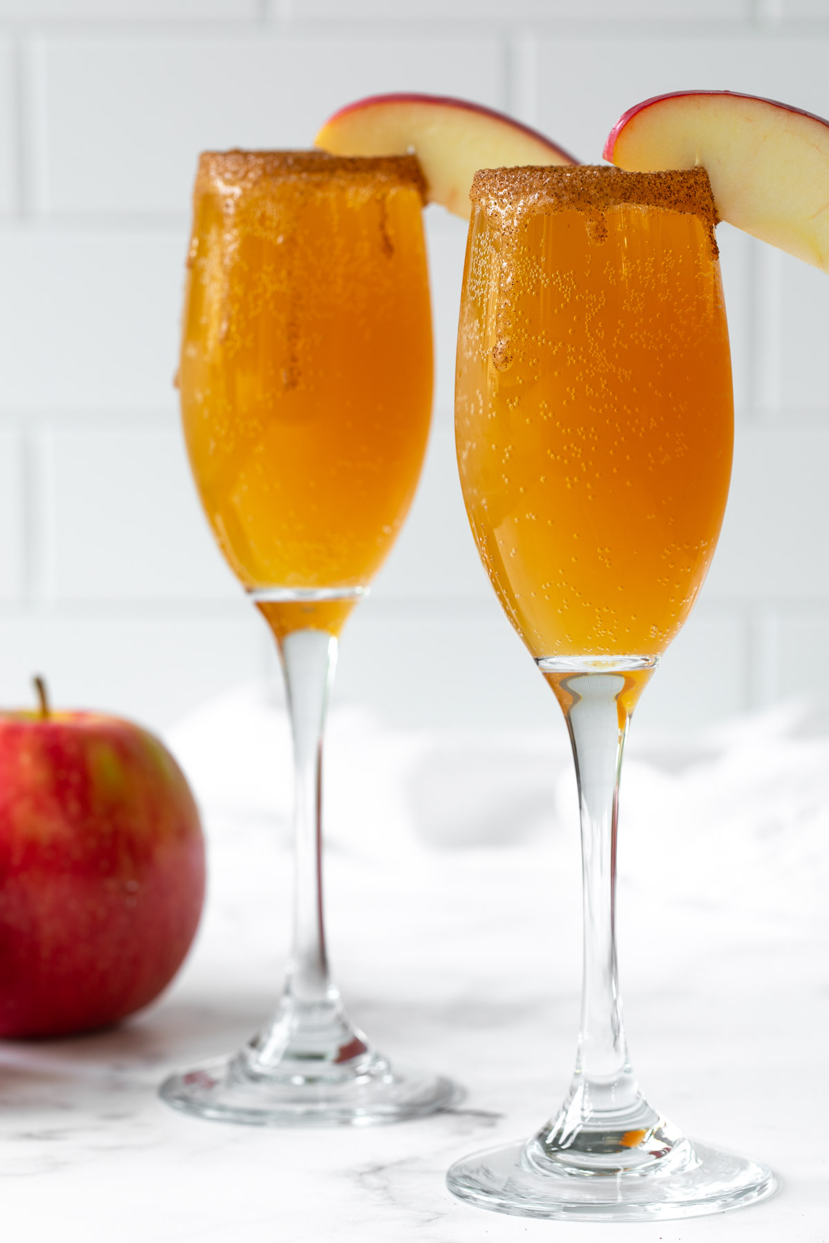 Front view of two caramel apple mimosas garnished with sliced apple.