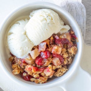 Overhead closeup view of a bowl of cranberry apple crisp with vanilla ice cream.